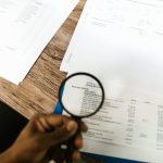 A hand using a magnifying glass to review property documents